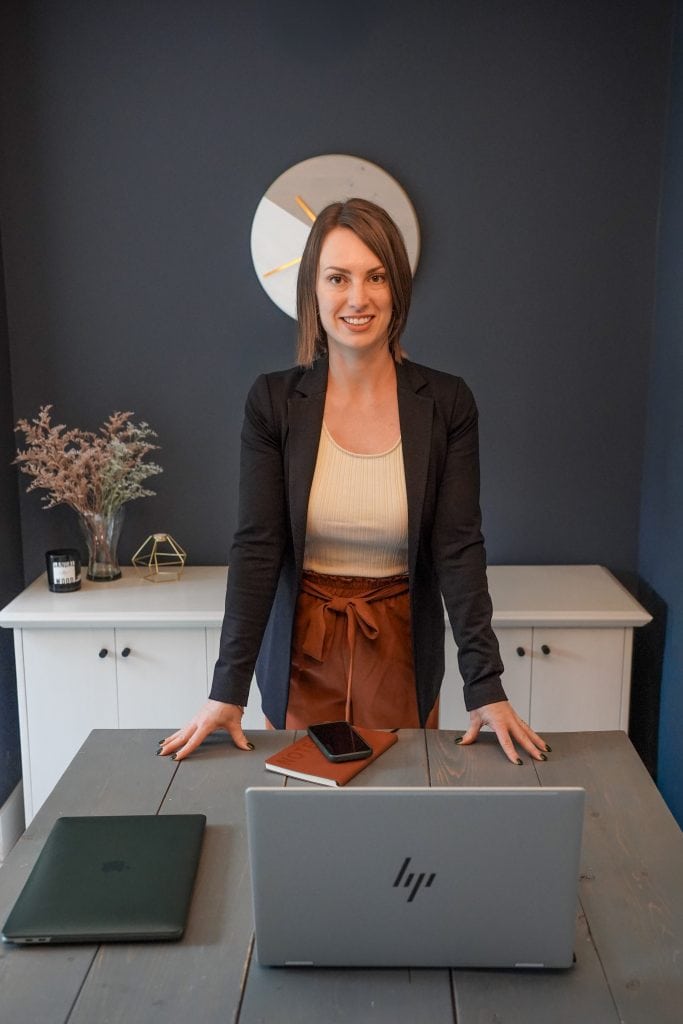 business woman standing behind a dining room table in front of a laptop