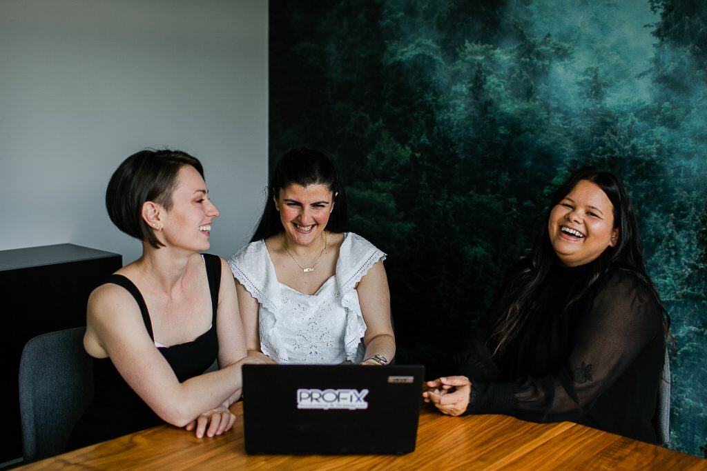 three women smiling around a table in front of a laptop, business consulting for small business growth